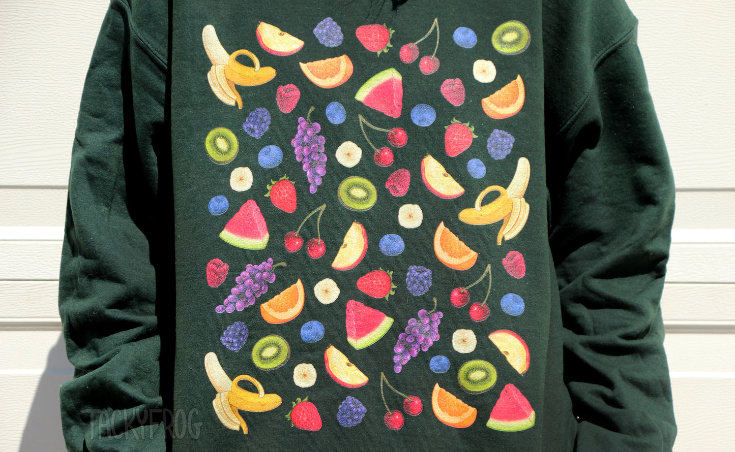 The fruits depicted on the sweatshirt are as follows: bananas, apple slices, blackberries, strawberries, cherries, blueberries, kiwi slices, orange slices, watermelon slices, grapes, and raspberries.