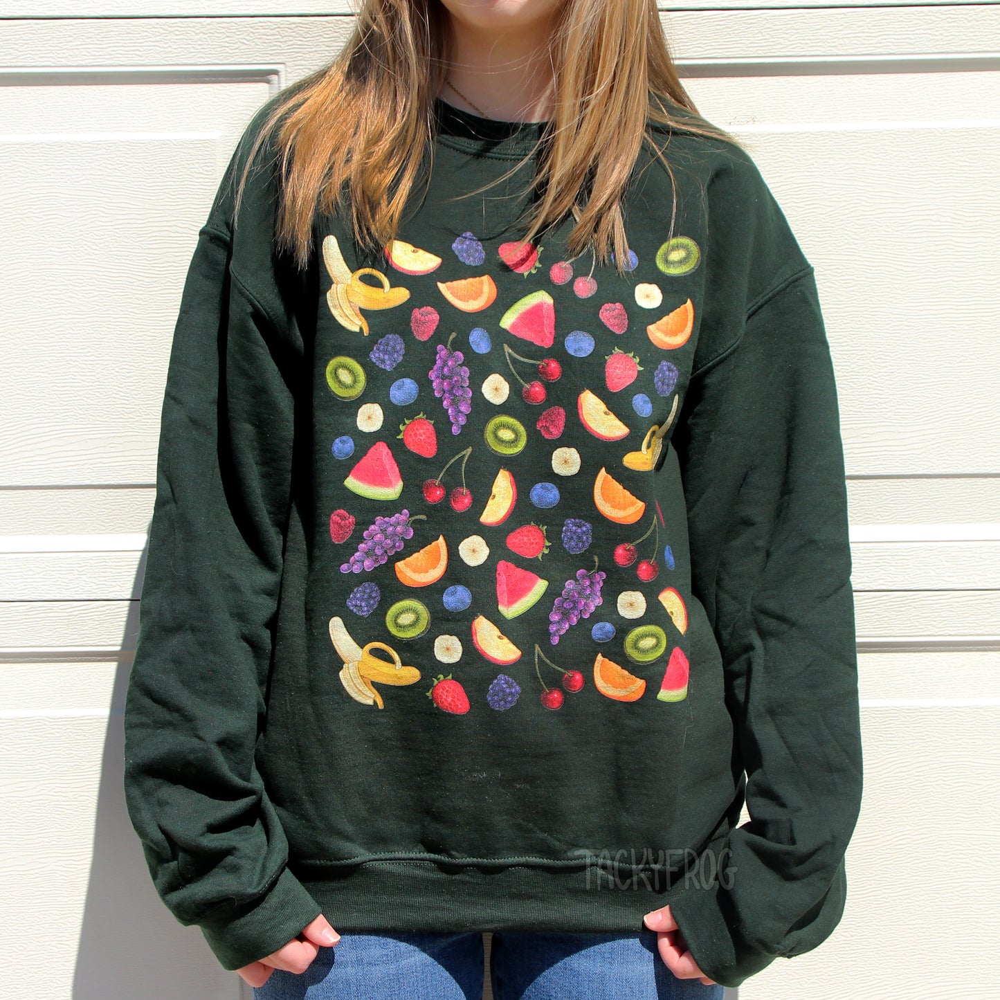 A woman wearing a forest green-colored sweatshirt featuring a design of various fruits. including berries.