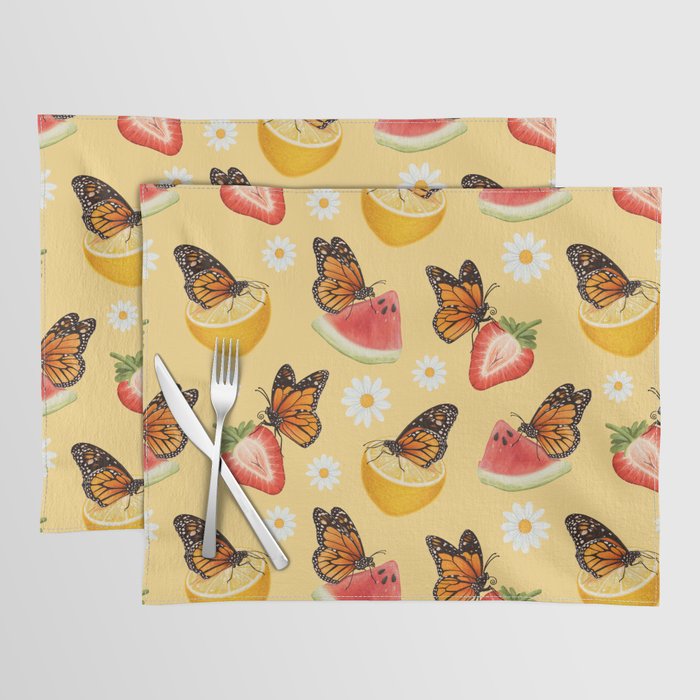 Two yellow placemats featuring a pattern made up of monarch butterflies, daisies, and fruit slices