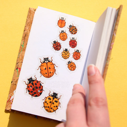 A sketchbook that is opened to show two different stickers. One sticker depicts eight smaller ladybugs, while the other sticker depicts three larger ladybugs.