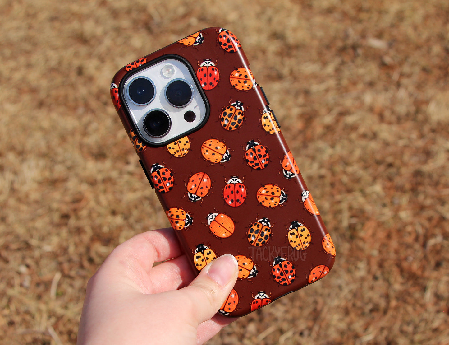 The ladybug tough phone case held above dead grass.