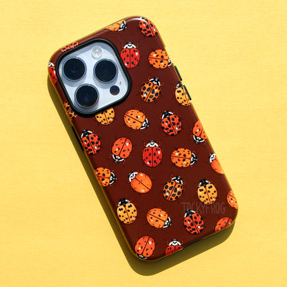 A brown phone case featuring a pattern of various ladybugs, shown on a light silver-colored phone.