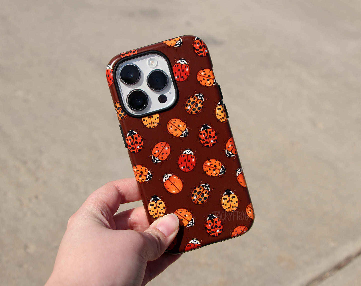 The ladybug phone case held above concrete.