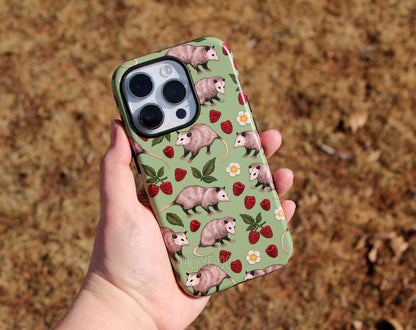 The opossum-patterned phone case held above the ground. It is shown on a white-colored phone.