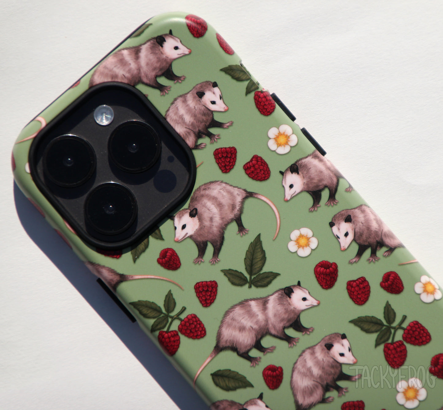 A closeup of the details on the opossum phone case, shown on a dark grey phone. The inner layer of the case is solid black. It is visible around buttons and openings. 