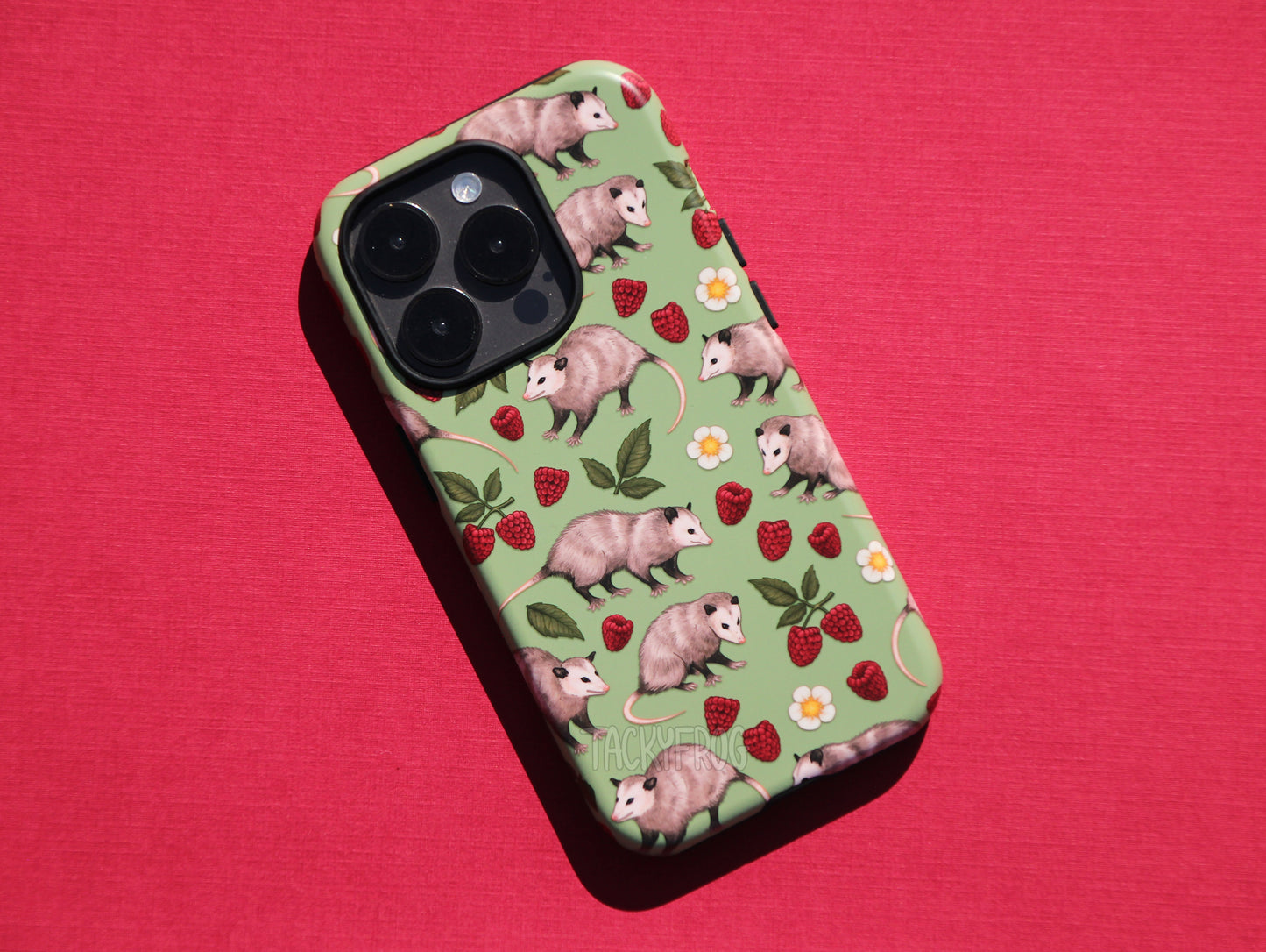 The opossum phone case pictured on a dark grey phone against a red background.