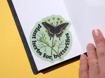 The "plant herbs for butterflies" sticker placed inside of a small sketchbook.
