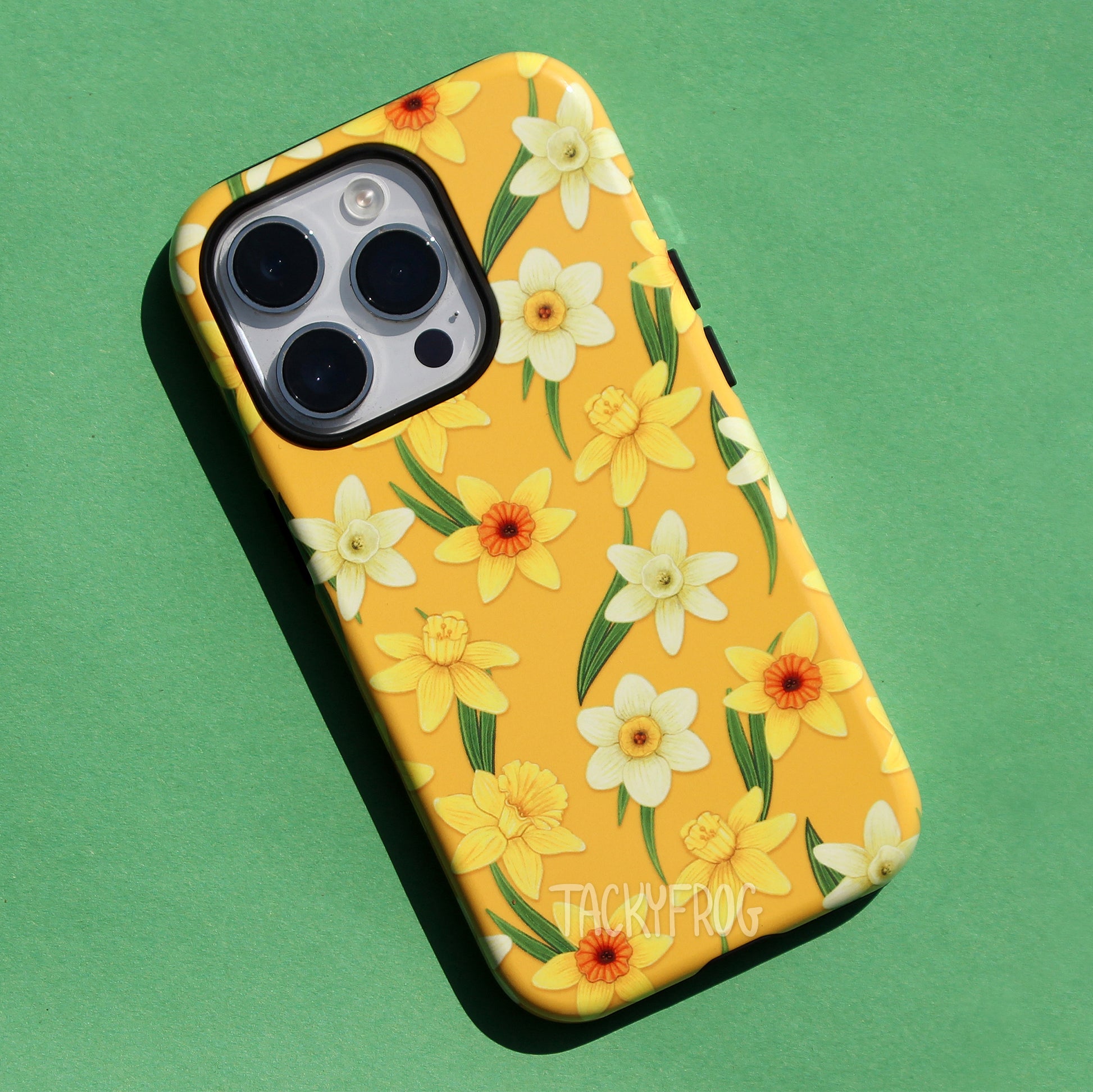 A yellow phone case featuring a pattern of yellow and white daffodils and green wispy leaves. The inner layer of the case is solid black.