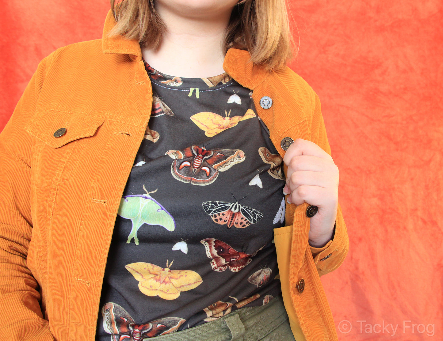 A brown t-shirt with a moth pattern on it, worn under an orange jacket.