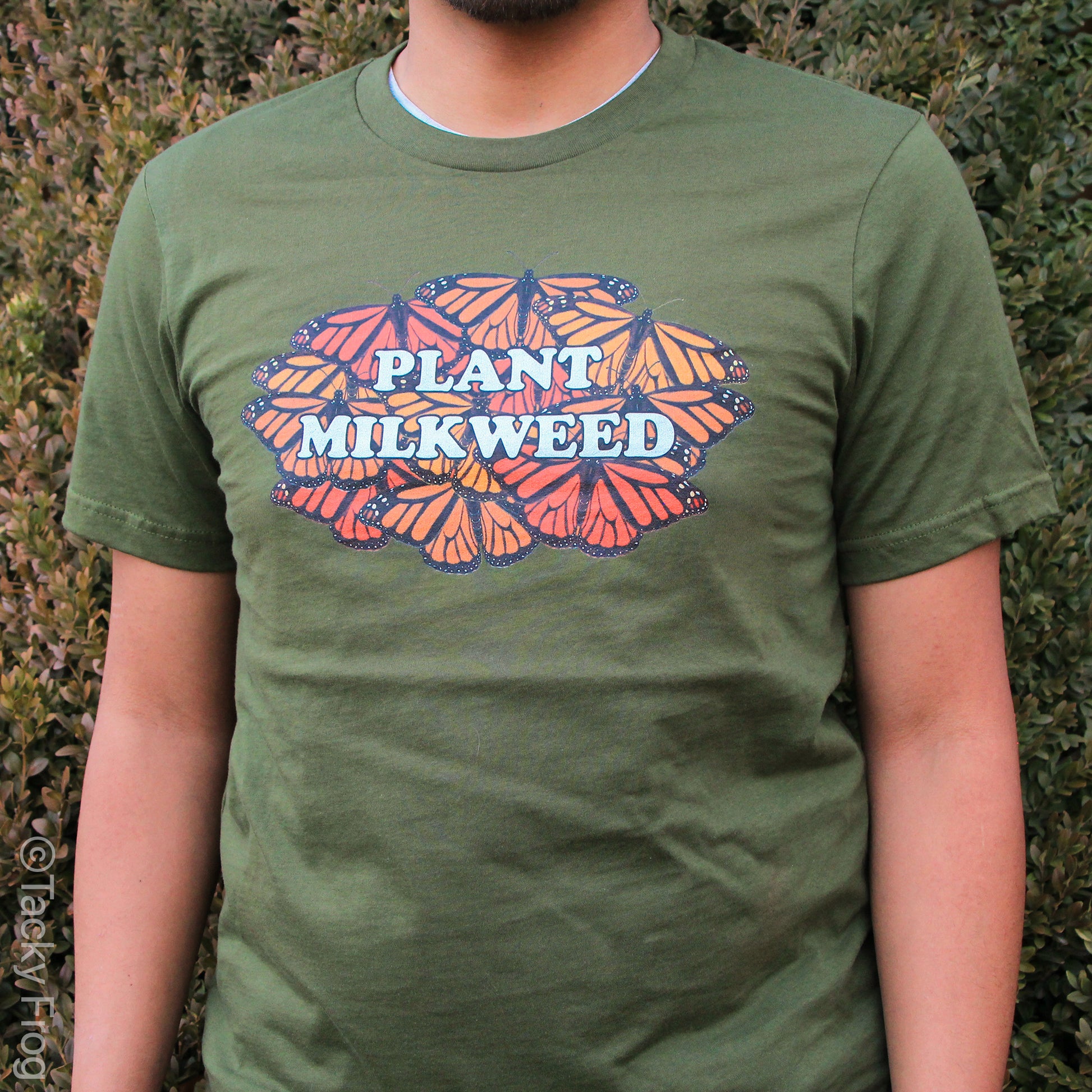 An olive green t-shirt featuring a monarch butterfly design that says "Plant Milkweed"