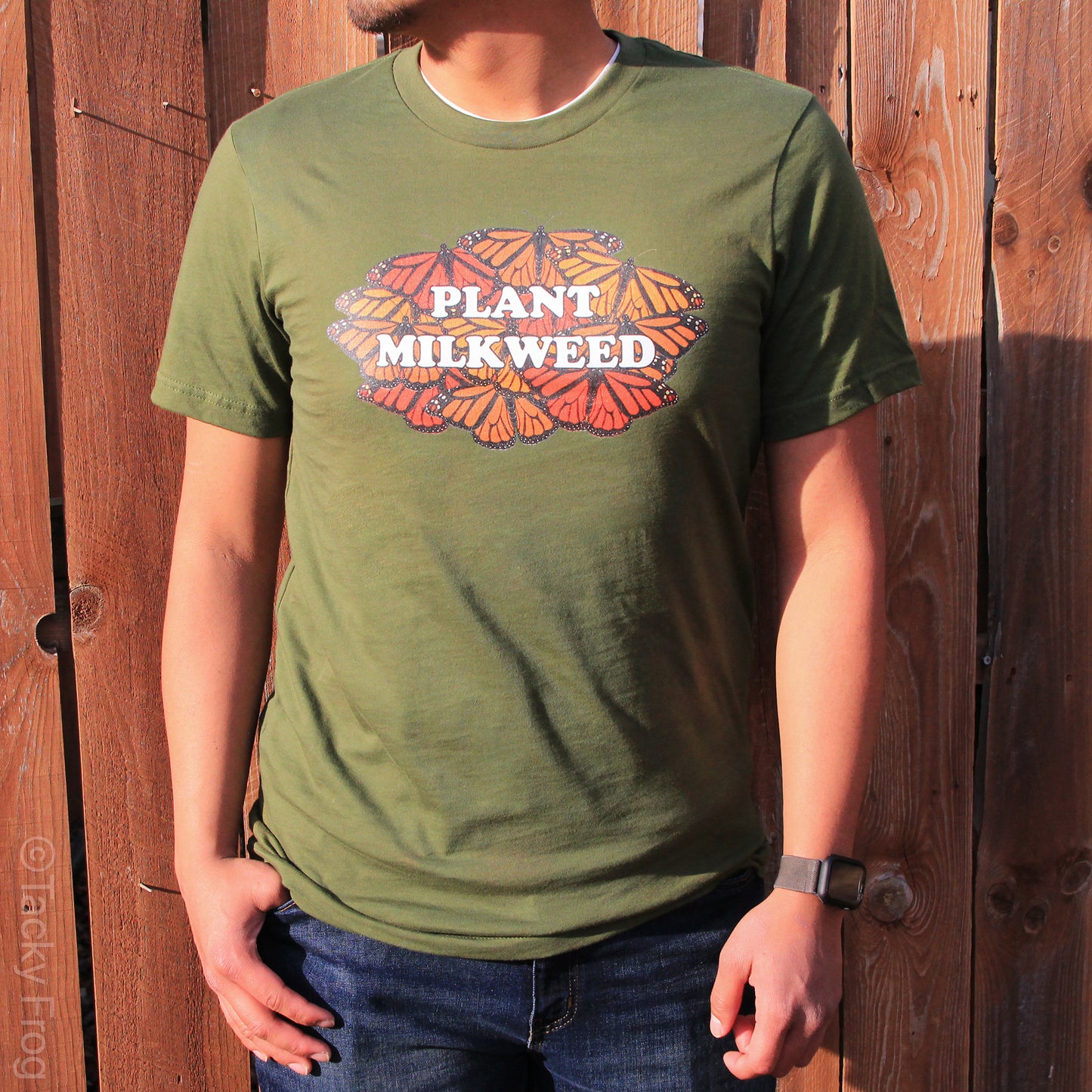 A man wearing an olive green shirt featuring a monarch butterfly design that says "Plant Milkweed"