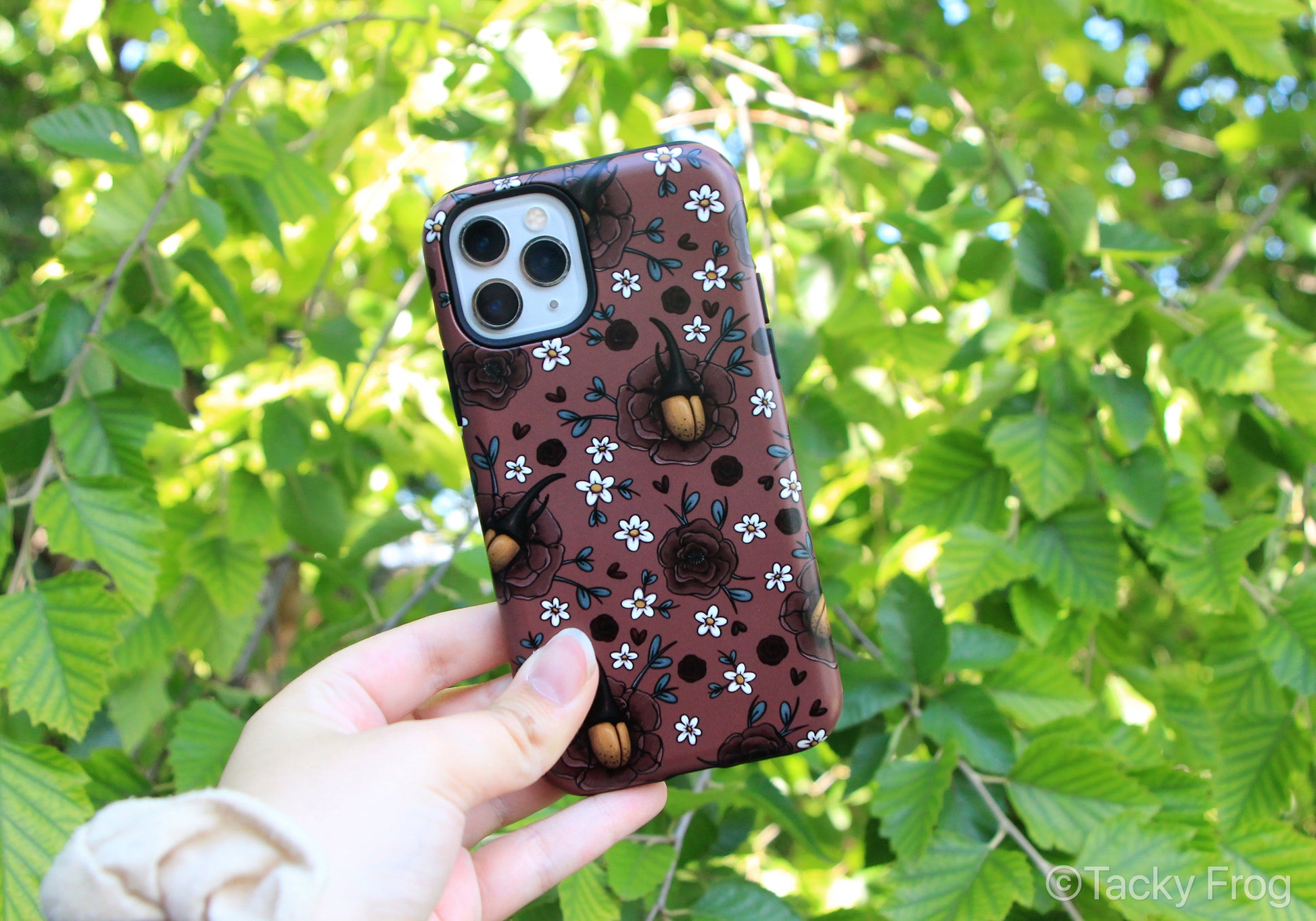 Floral Hercules beetle phone case held up in front of a tree