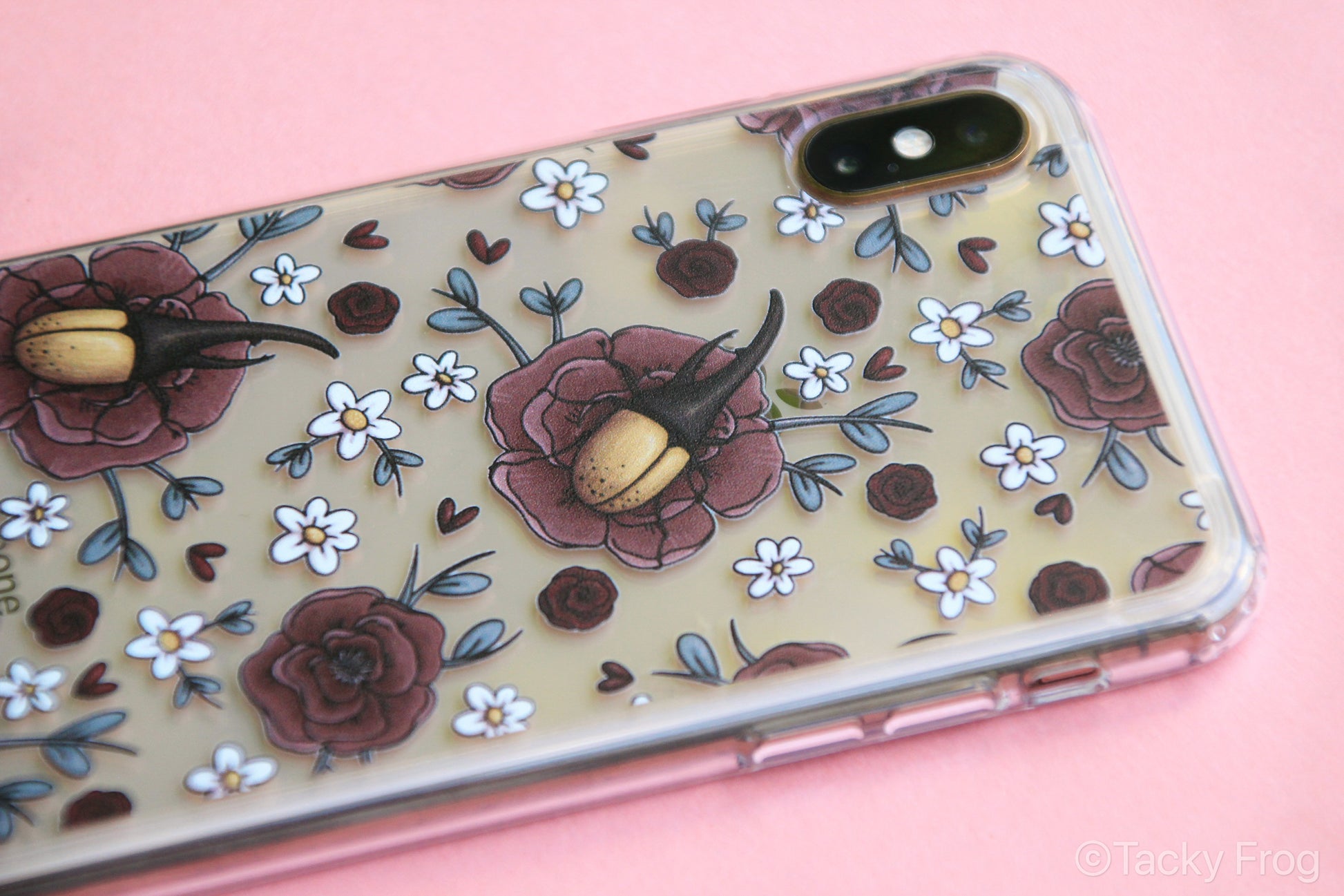 An angled view of the Hercules beetle and florals clear phone case, shown on a gold iPhone.