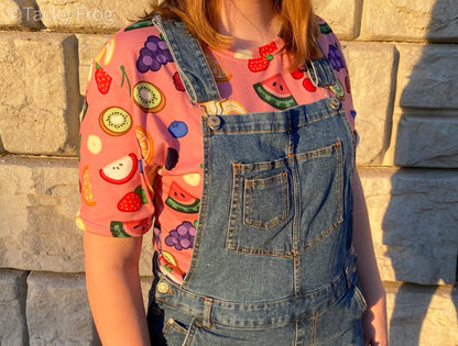 A woman wearing the fruit salad pattern t-shirt under overalls.