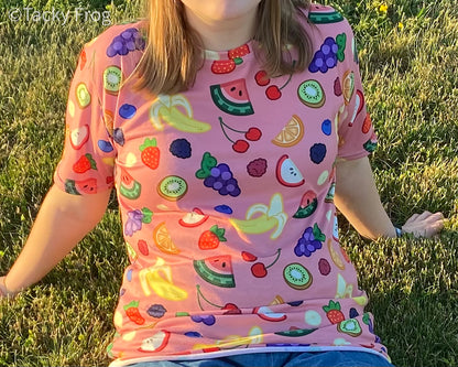 A woman wearing the fruit salad pattern t-shirt while sitting in the grass.