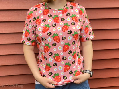 A woman wearing a pink shirt with daisies, strawberries, and bees on it.