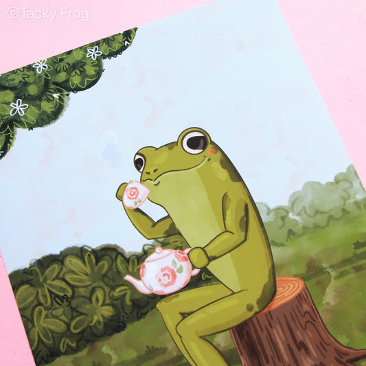 Close up of the details of the art print. The art print depicts a frog drinking tea while sitting on a tree stump.