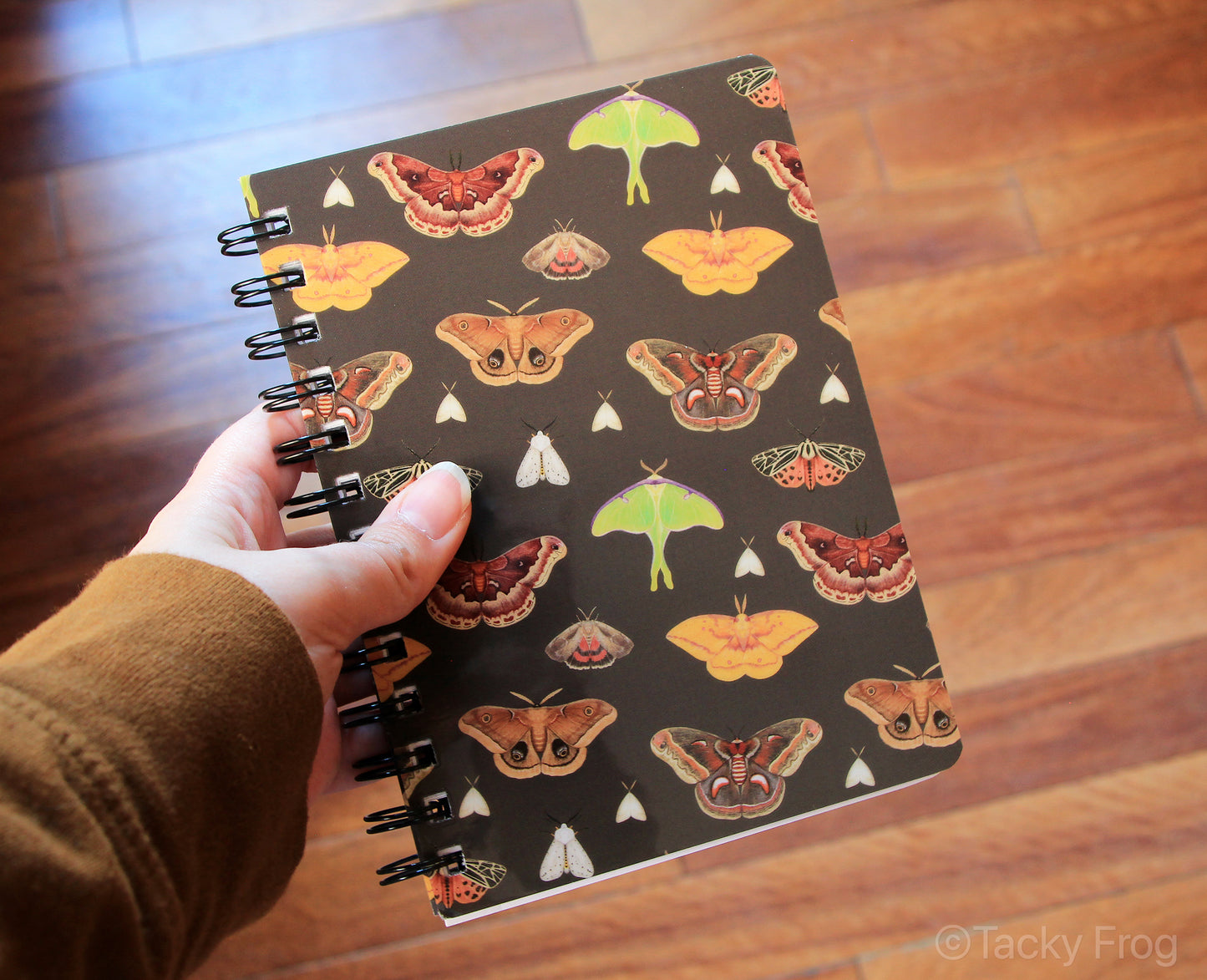 The moth pattern spiral notebook held in a hand for scale.