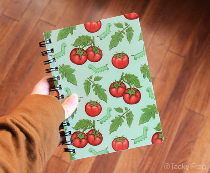 The tomato hornworm and tomato pattern notebook held in a hand for scale.