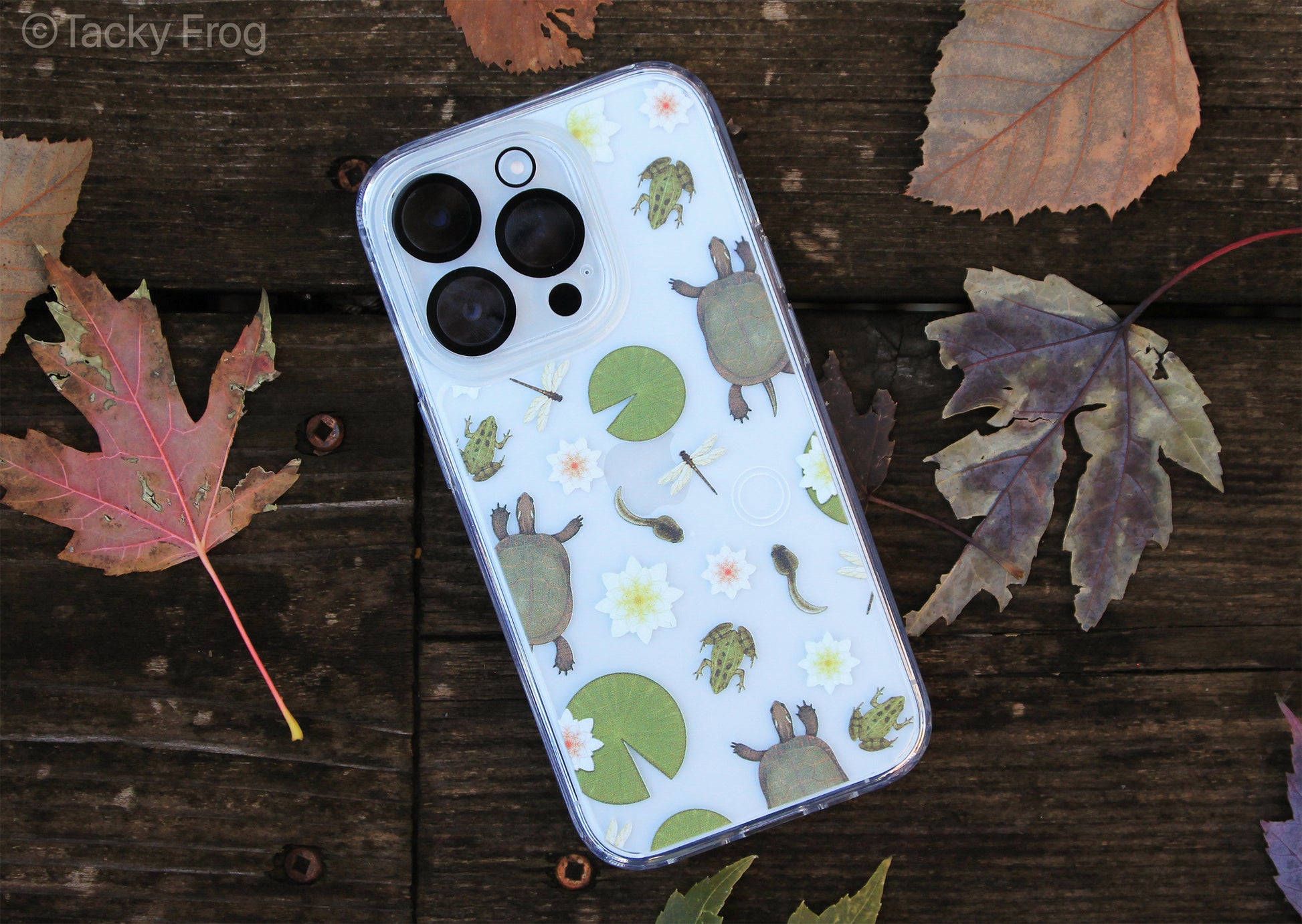 A clear phone case with lily pads, water lilies, turtles, frogs, tadpoles, and dragonflies on it. The camera protector is not included.