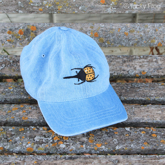 A light blue denim baseball cap with an embroidered Hercules beetle on it.