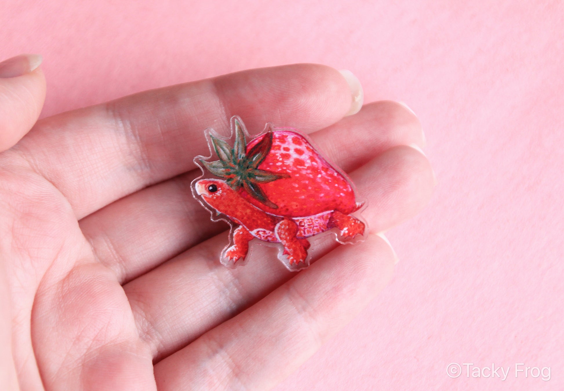 An acrylic strawberry turtle pin held in a hand for scale