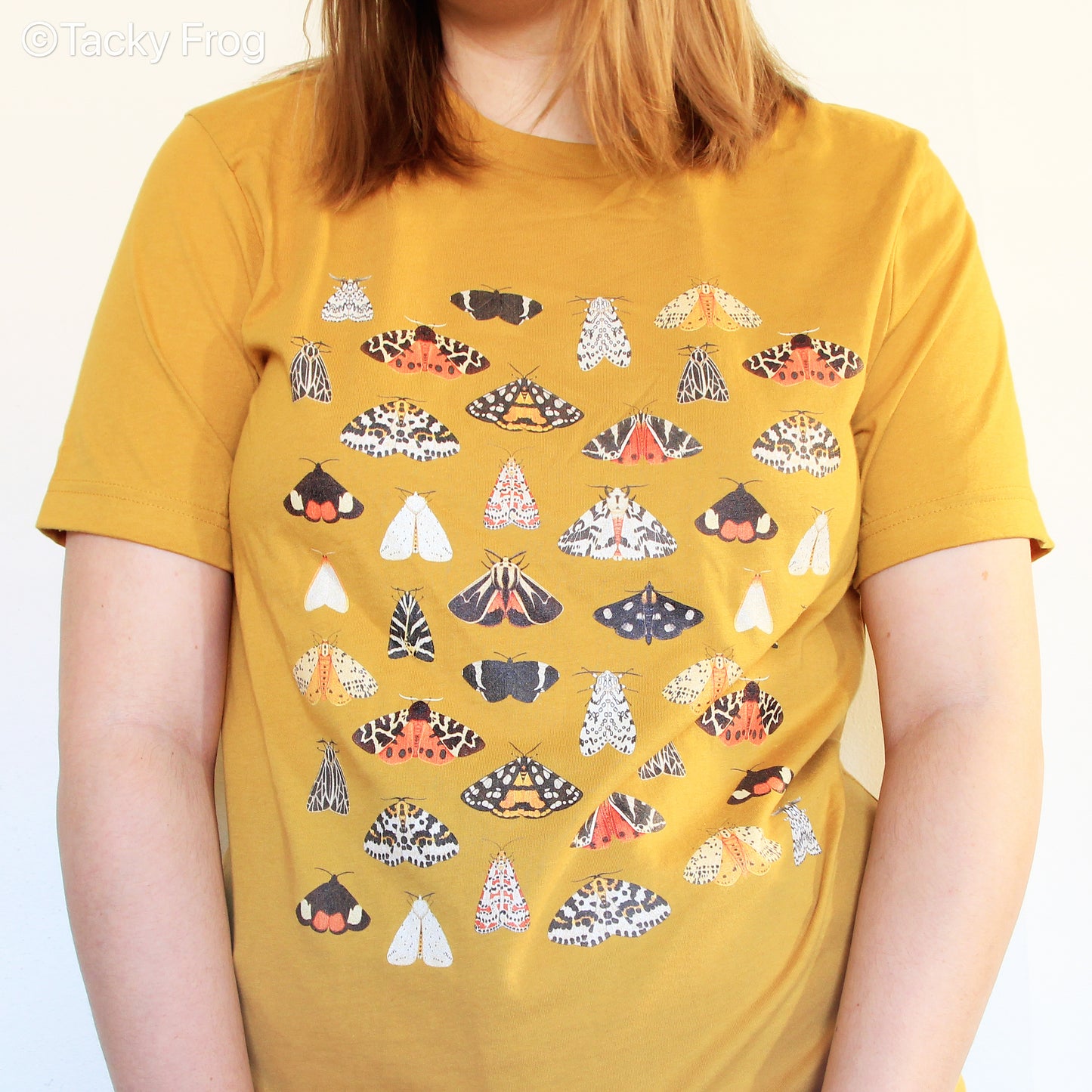 A woman wearing a mustard-colored t-shirt with various beautiful moth illustrations on it.