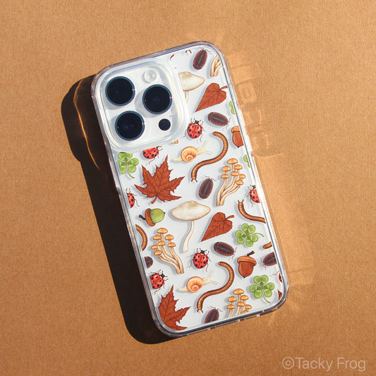 A clear phone case with a nature-inspired pattern on it, which includes illustrations of bugs, mushrooms, leaves, and acorns.