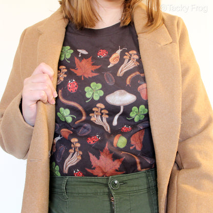 A woman wearing a brown t-shirt with various nature-inspired illustrations on it. She is wearing a light brown coat over the shirt.