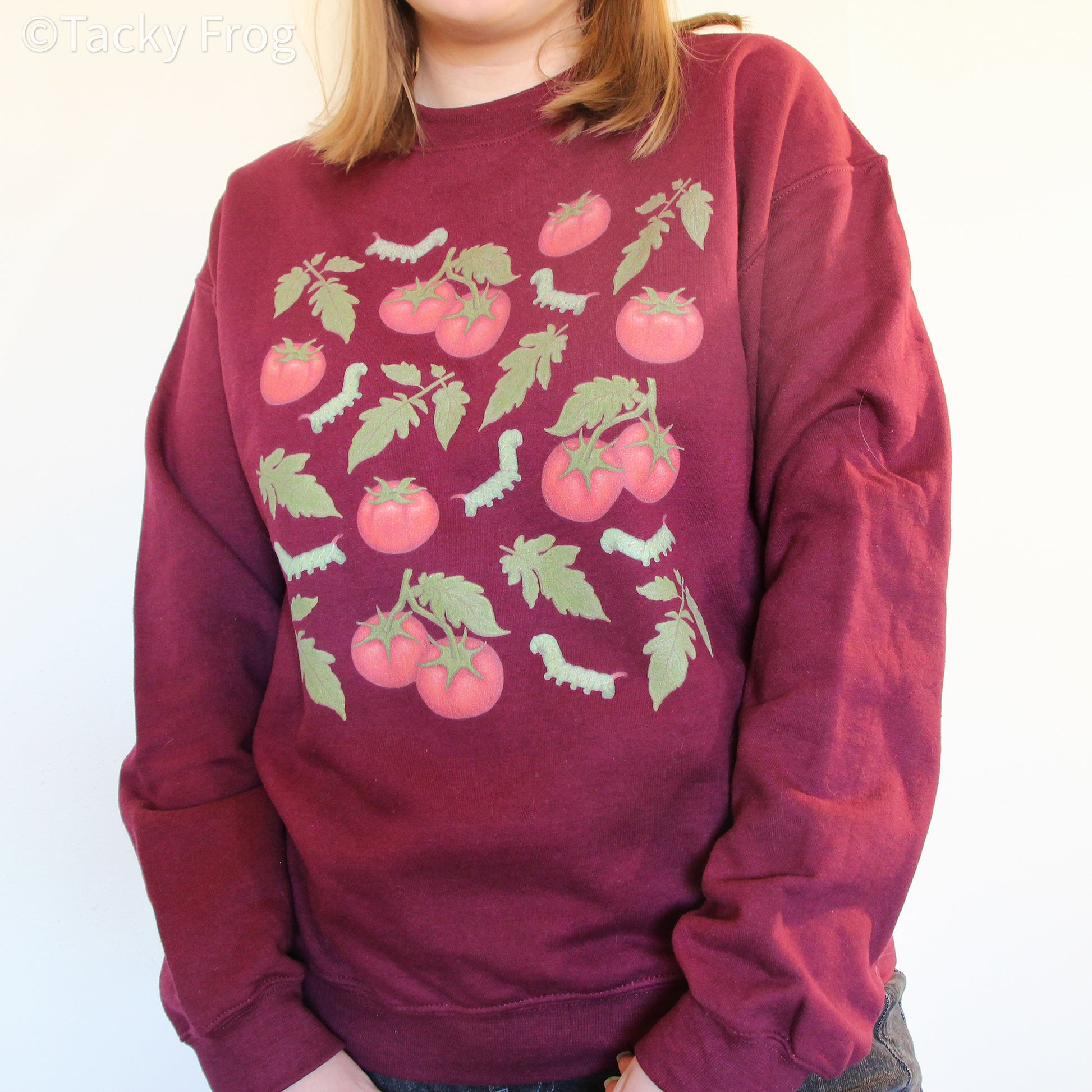 A woman wearing a sweatshirt with caterpillars, tomatoes, and leaves on it.