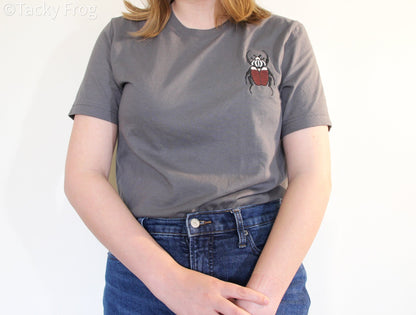 A woman wearing a grey t-shirt with a Goliath beetle embroidered on it. She is wearing the shirt tucked-in.