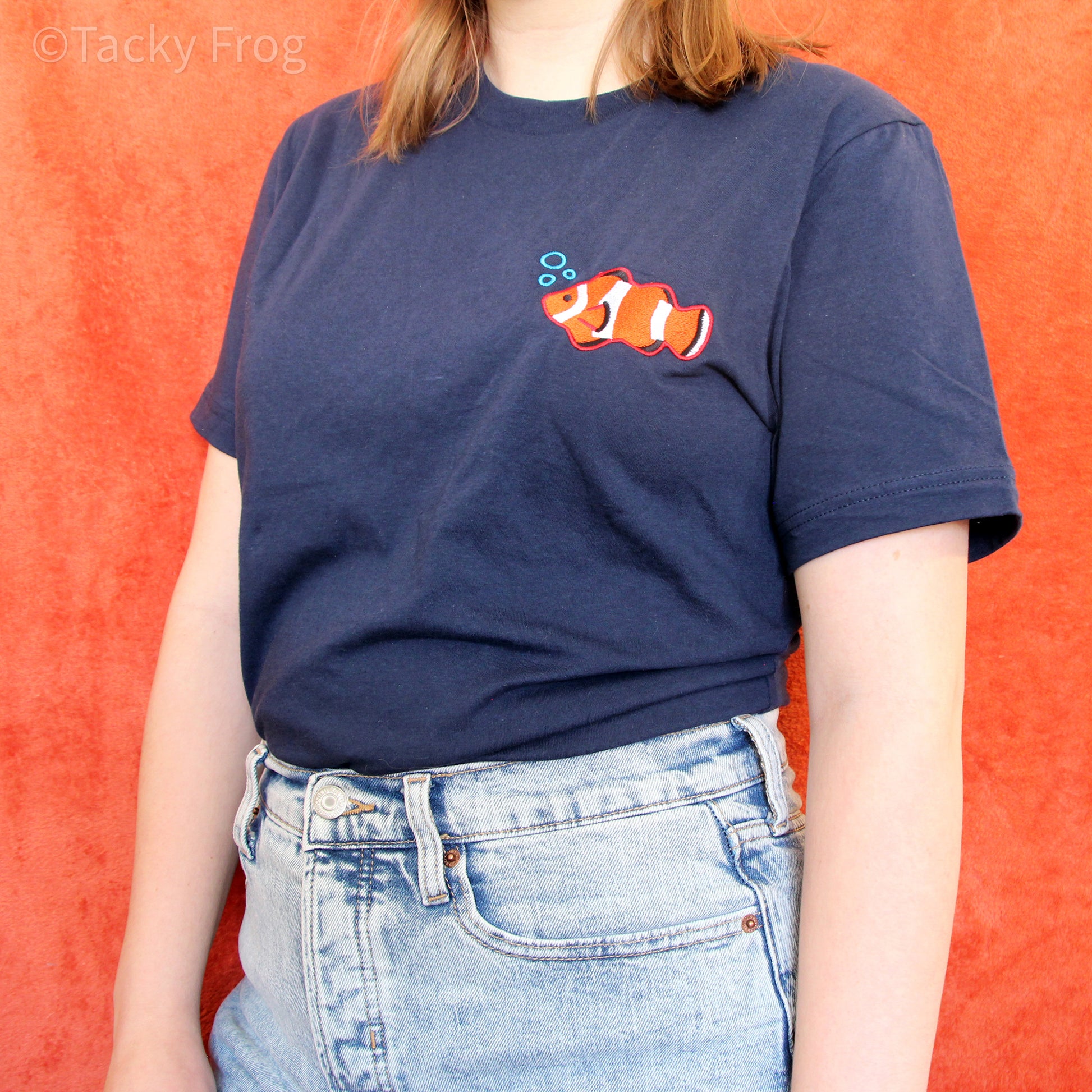 A woman wearing a tucked-in shirt with a clownfish embroidered on it.