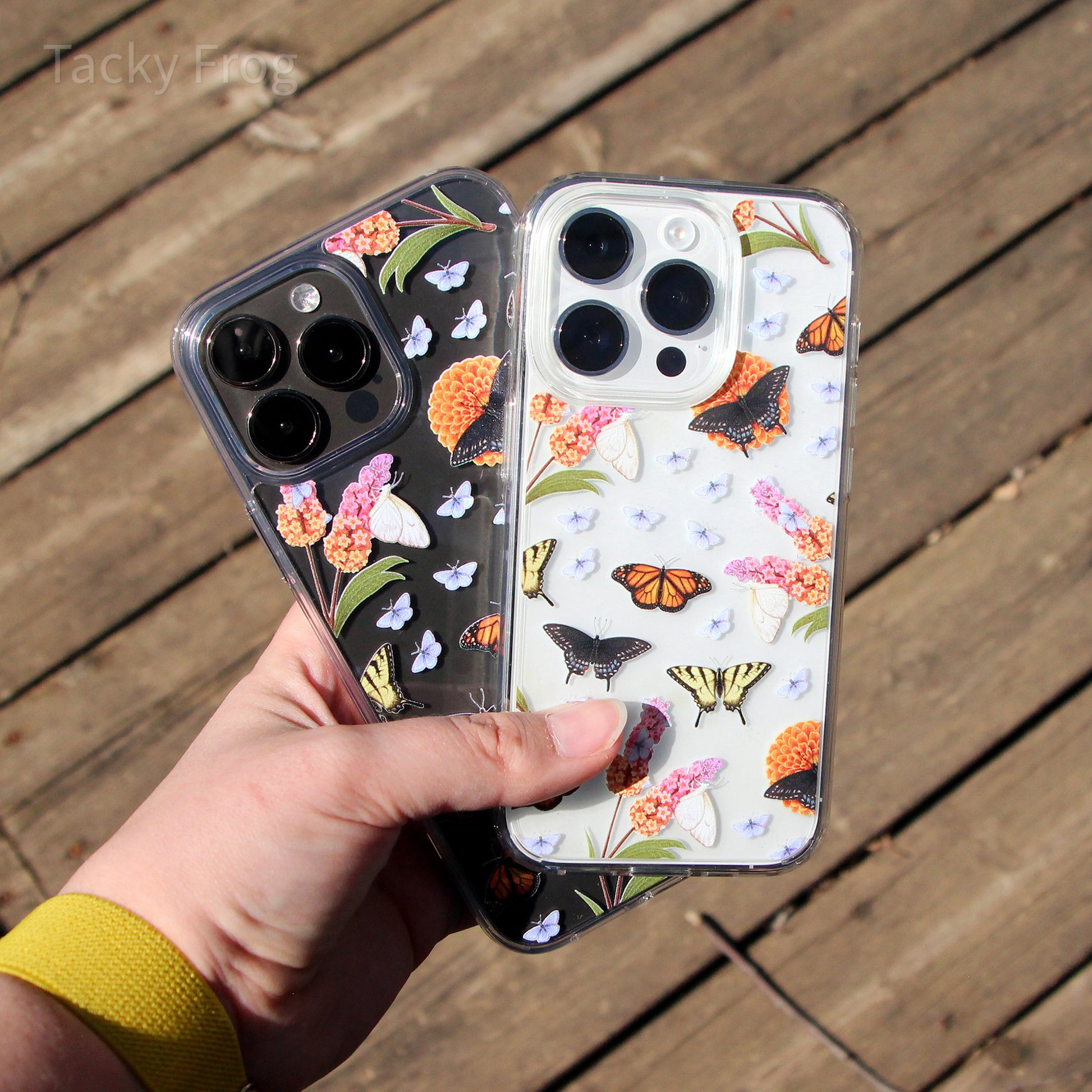 A hand holding two different sizes of the butterfly garden case on two different colored phones.