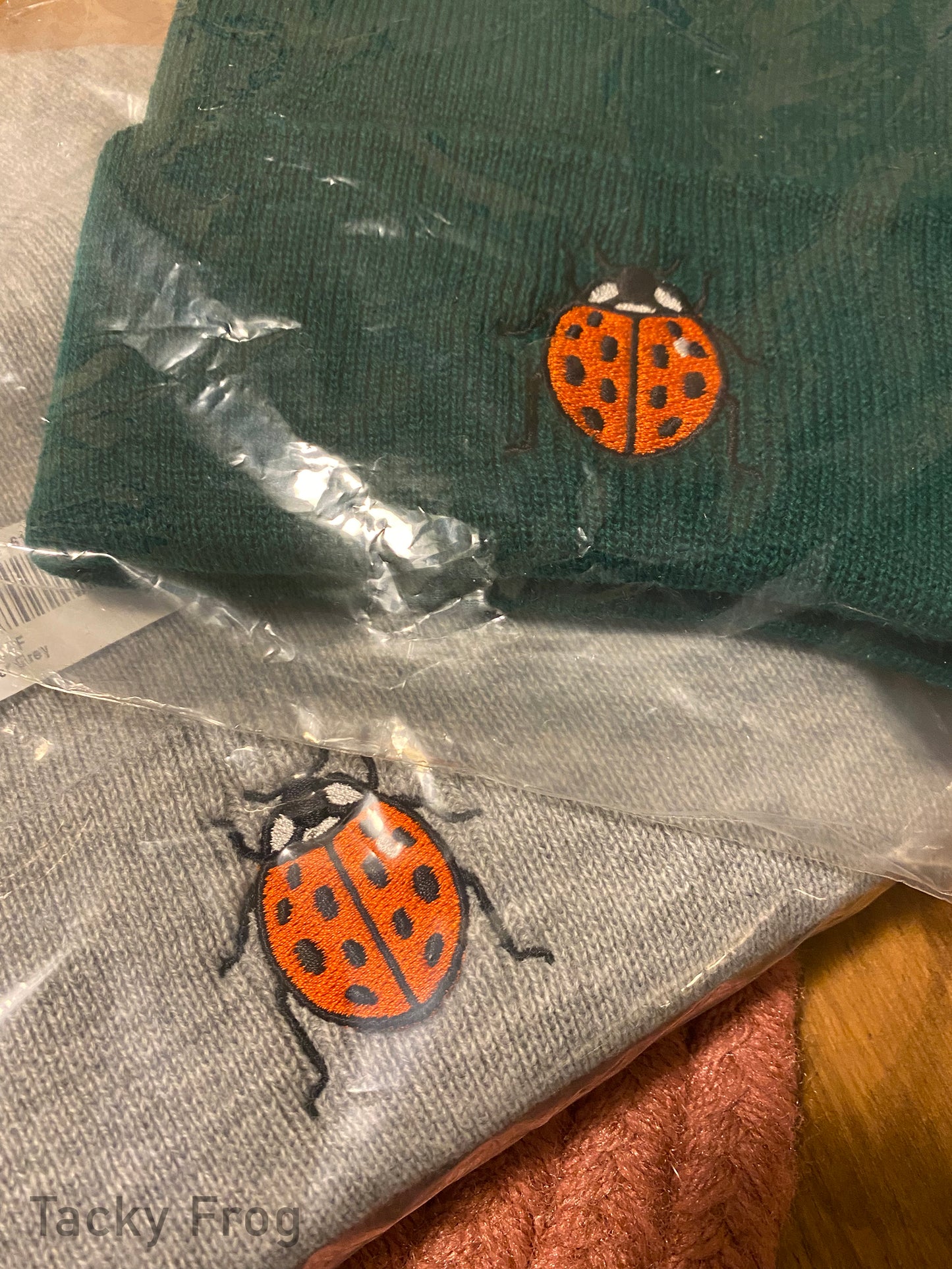 The heather grey and spruce colored ladybug beanies wrapped in plastic.