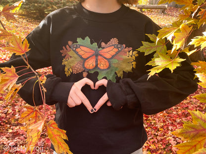 A girl wearing a black sweatshirt with a monarch butterfly and autumn leaves on it.