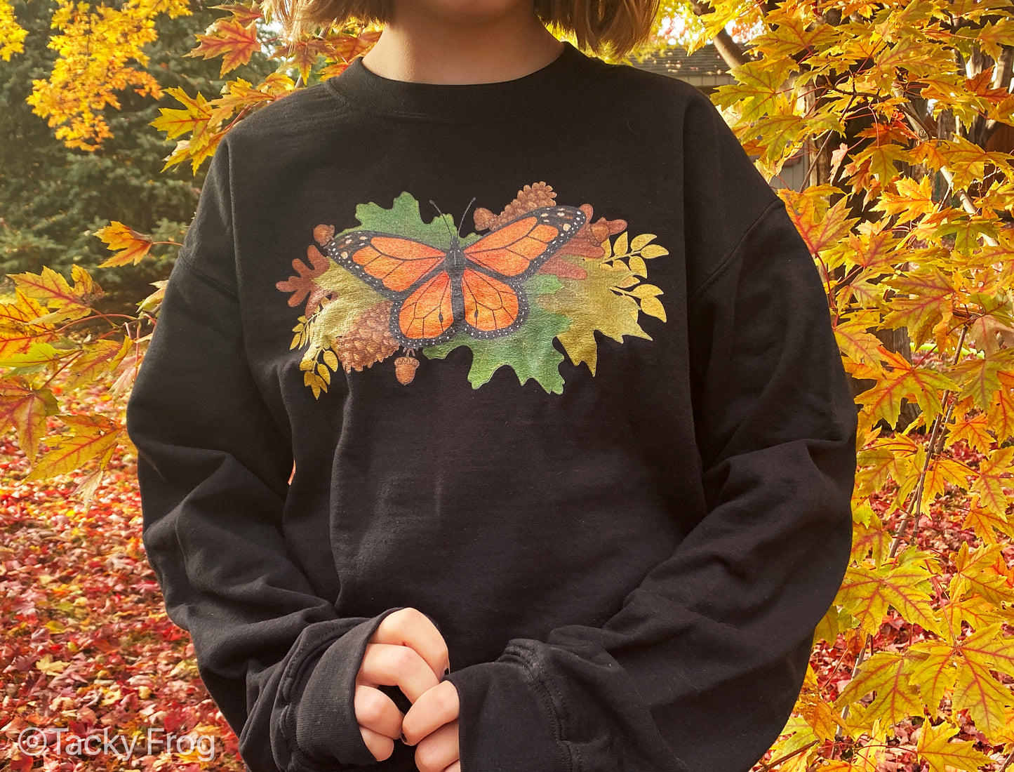 A girl wearing a black sweatshirt with a monarch butterfly and autumn leaves on it.