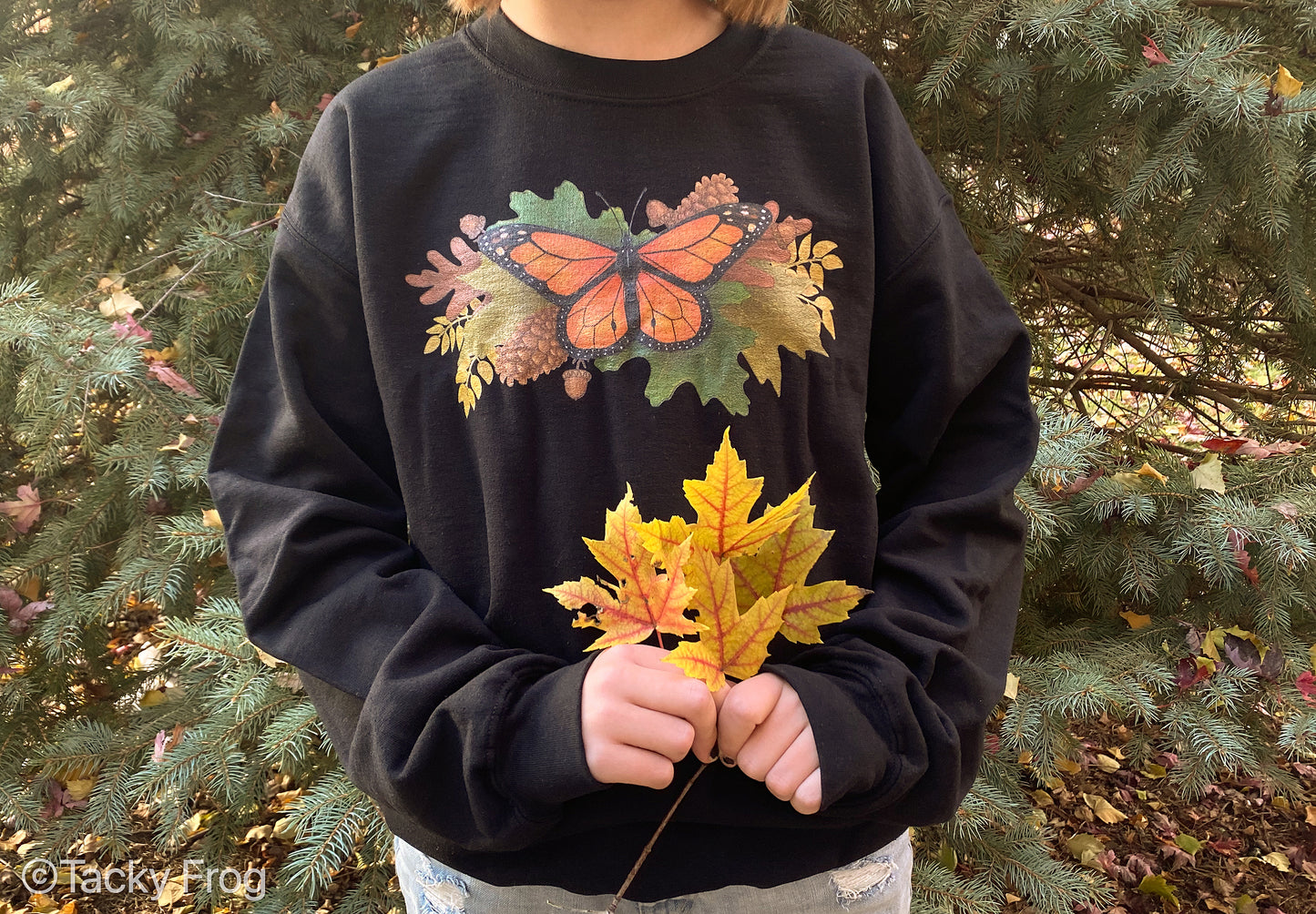 A girl wearing a black sweatshirt with a monarch butterfly and autumn leaves on it.