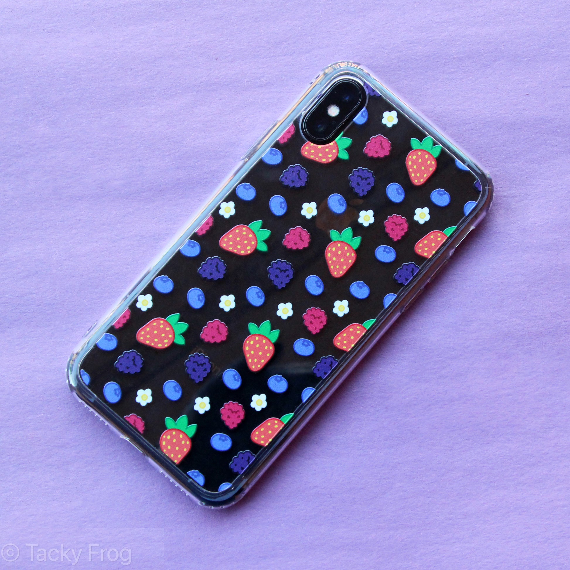 A clear phone case with a mixed berries and daisies pattern. It is shown on an iPhone X.