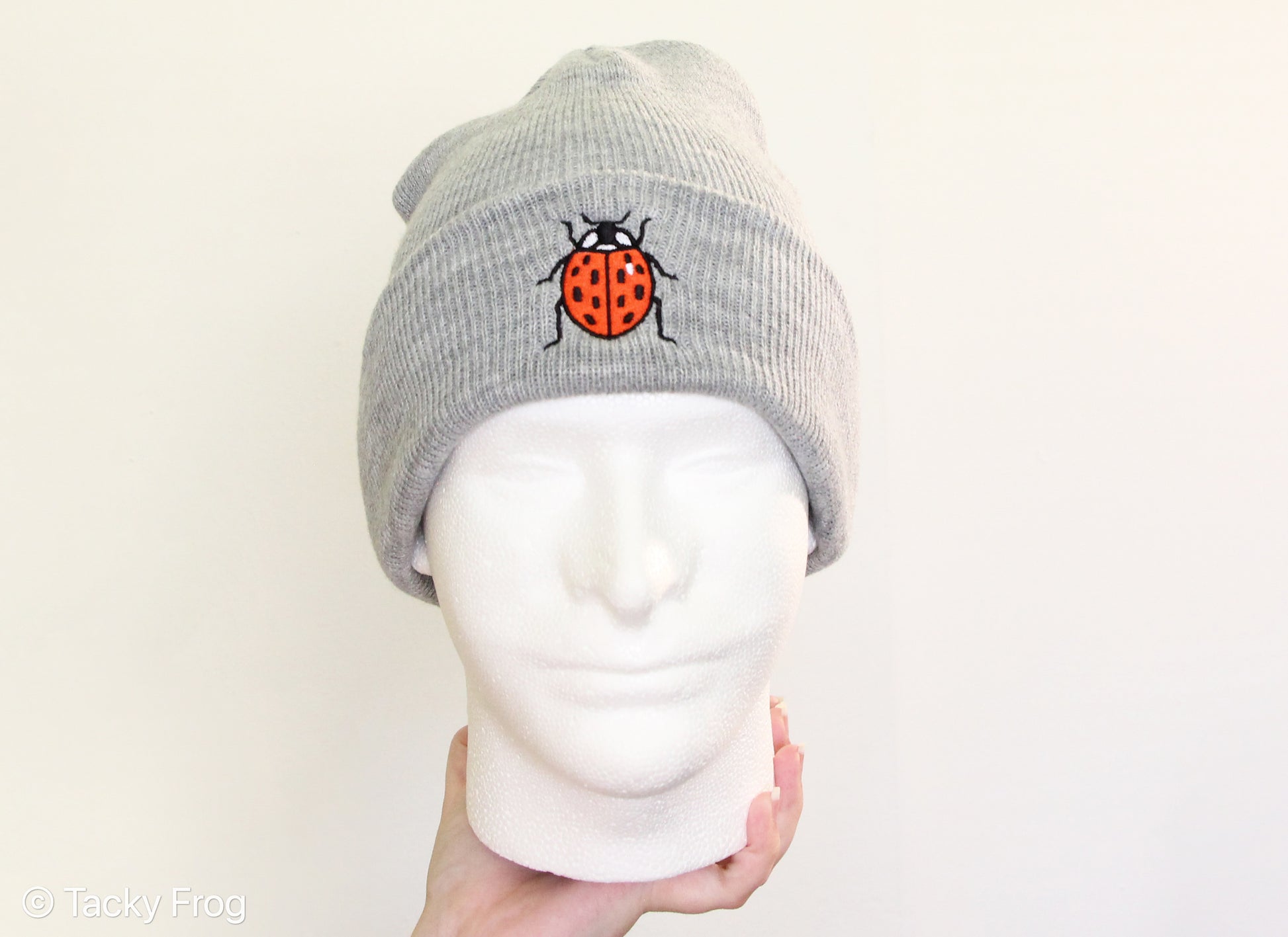 A foam head wearing a heather grey ladybug beanie.