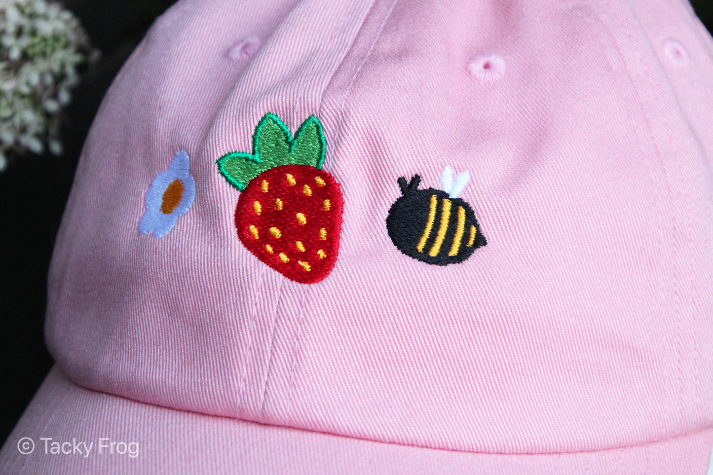 A closeup of the embroidery on the pink strawberries and bees dad hat.