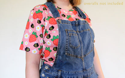 The strawberries and bees all over print shirt worn under overalls. Overalls are not included with your purchase.