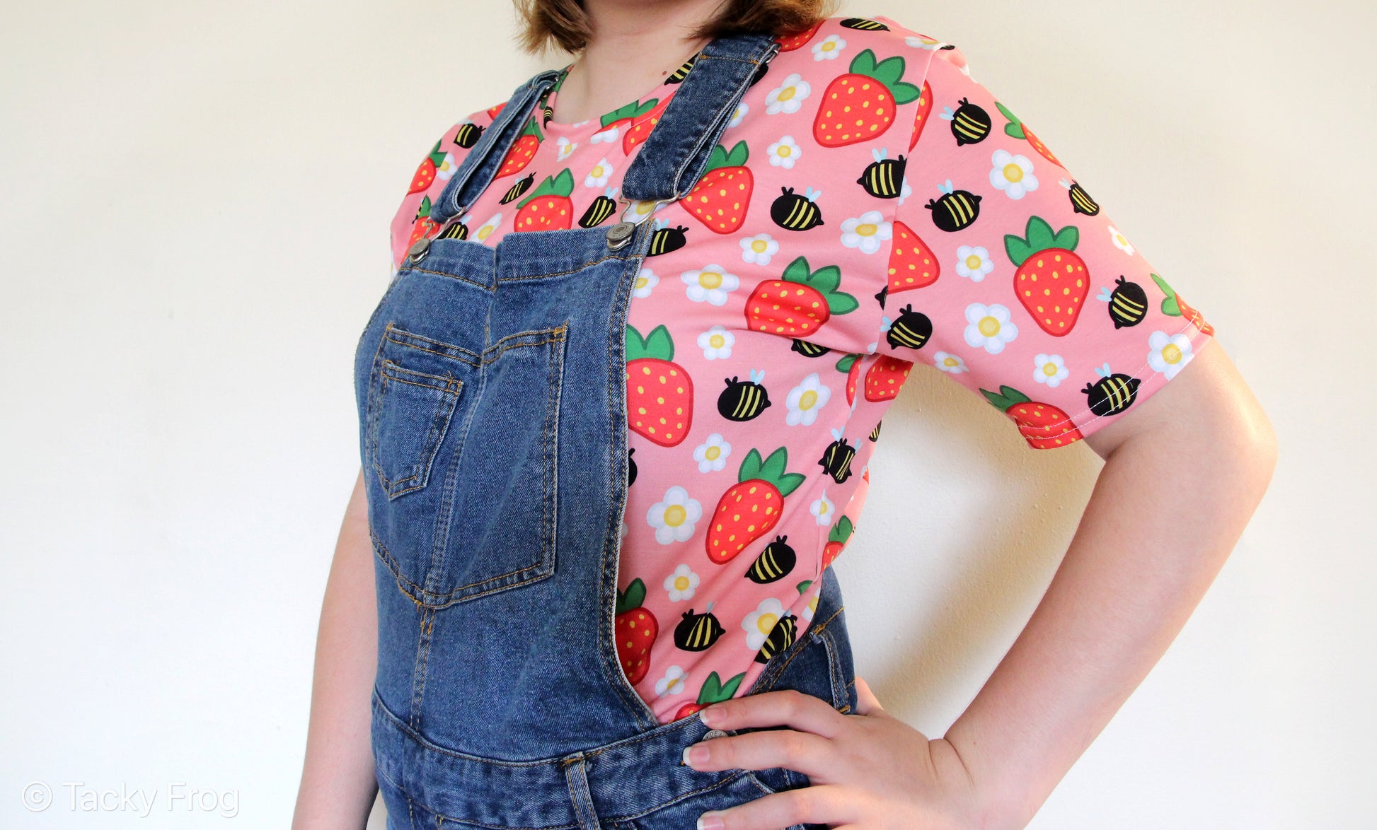 The strawberries and bees all over print shirt worn under overalls. Overalls are not included with your purchase.