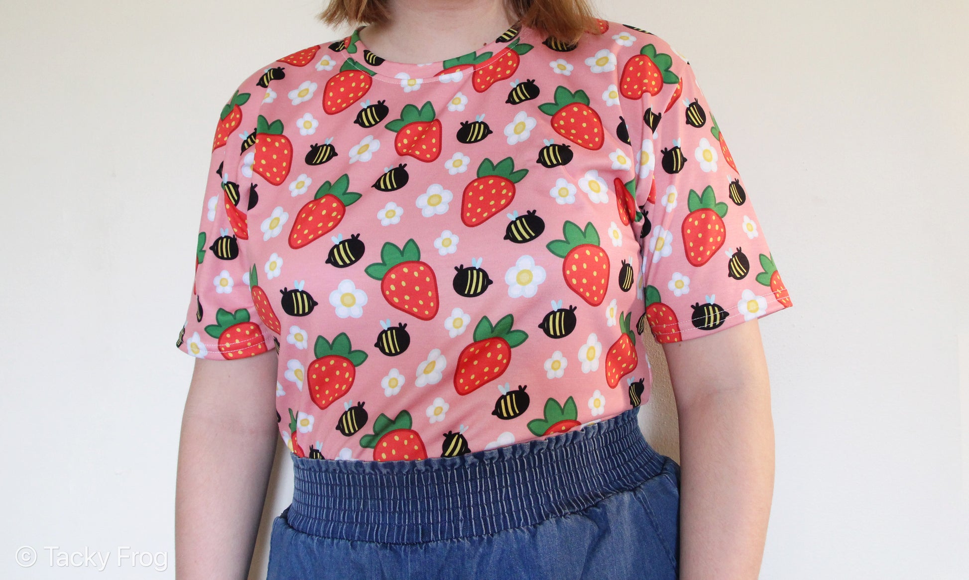 A woman wearing a pink shirt with daisies, strawberries, and bees on it.