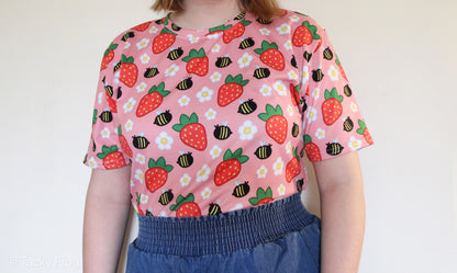 A woman wearing a pink shirt with daisies, strawberries, and bees on it.