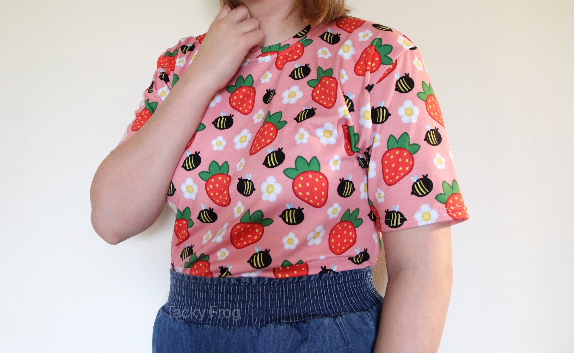 A woman wearing a pink shirt with daisies, strawberries, and bees on it.  Edit alt text