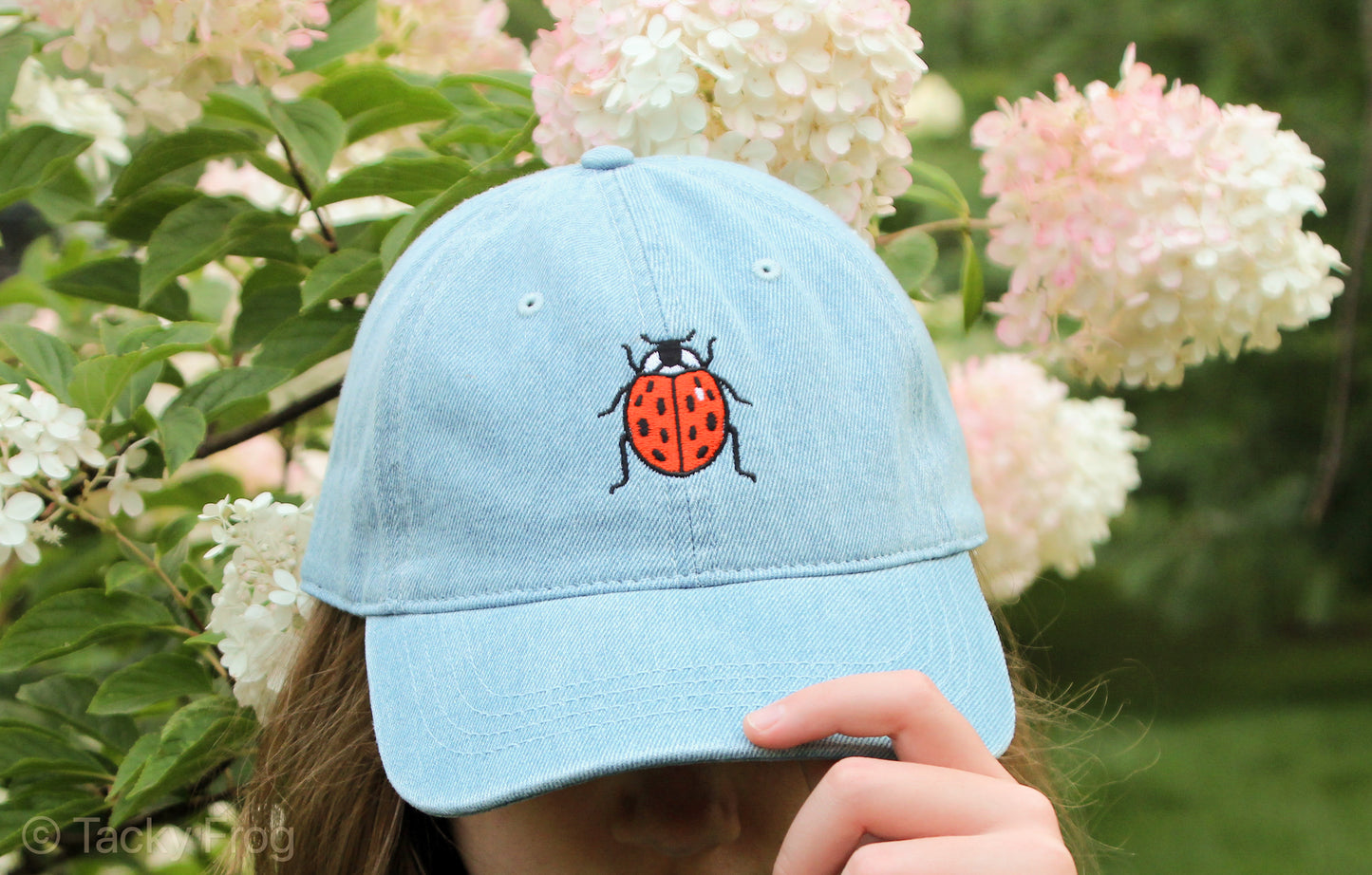 A girl wearing a light blue denim baseball cap with a ladybug on it.