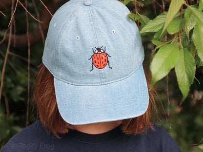 A light blue denim baseball cap with a ladybug on it.