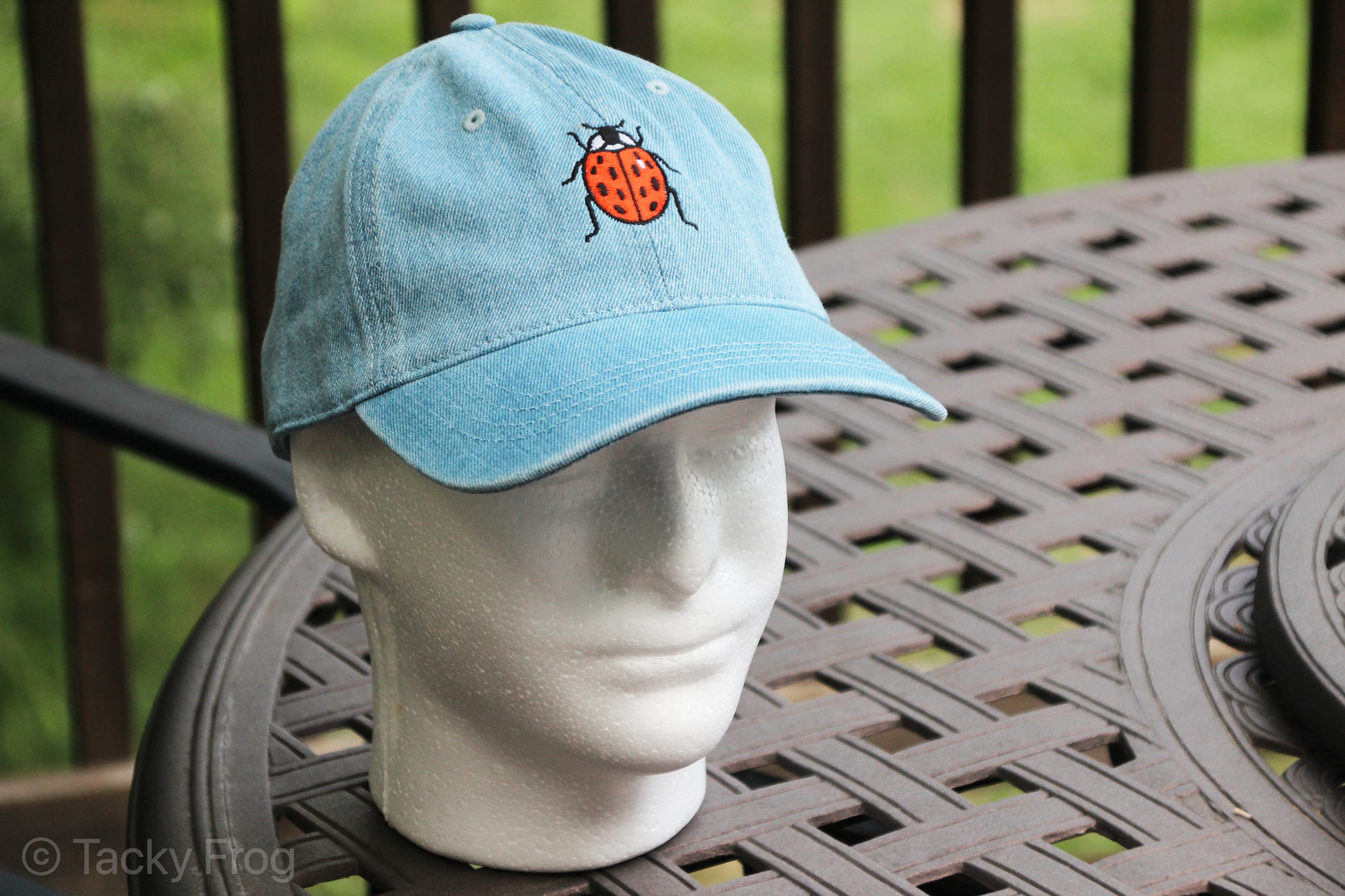 A foam mannequin head wearing a denim baseball cap with a ladybug on it.