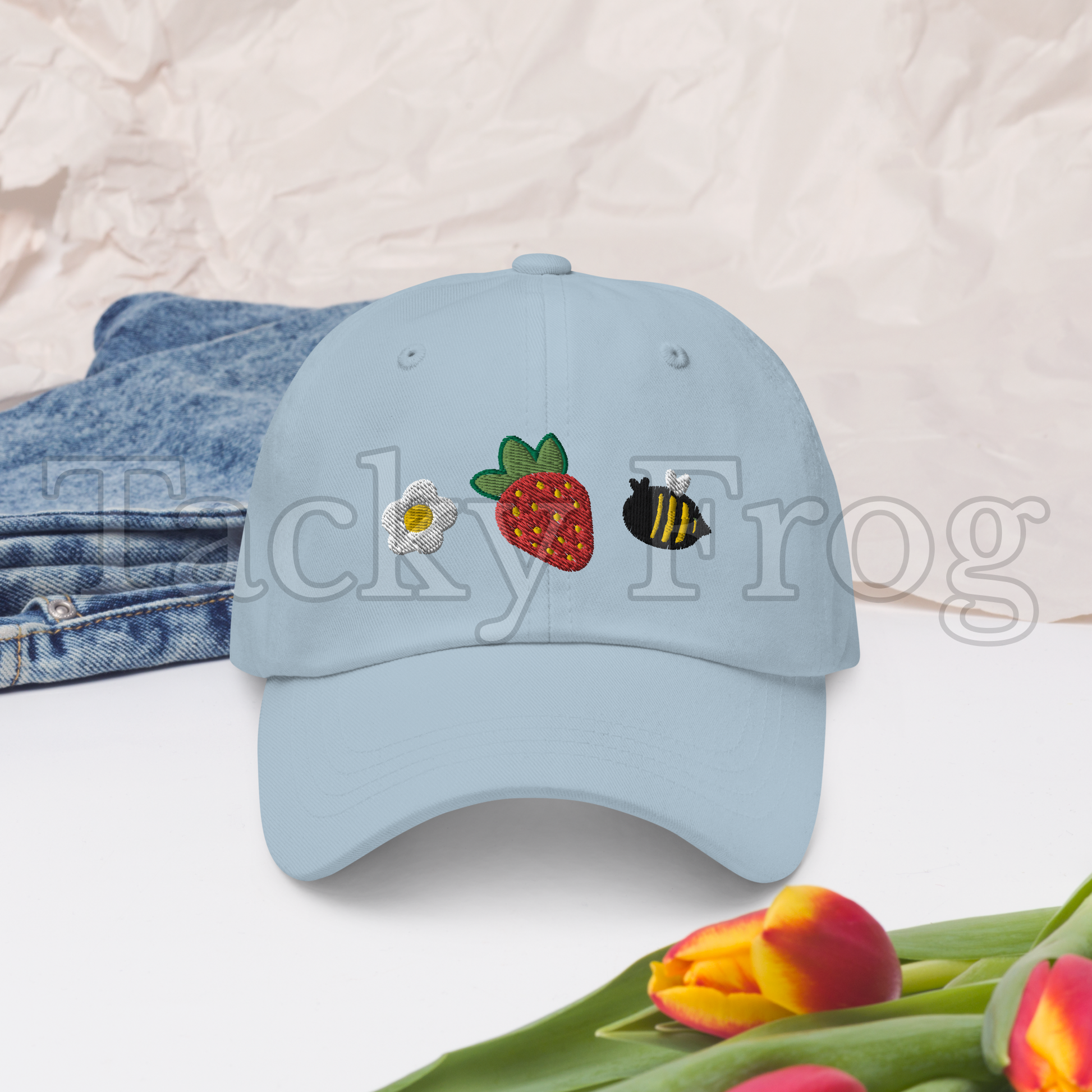 A mockup of the light blue strawberries and bees embroidered hat. There is a watermark over the image.