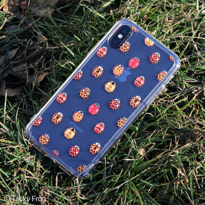 A clear phone case placed in the grass. The case has a ladybug pattern on it. It is shown on an iPhone X.